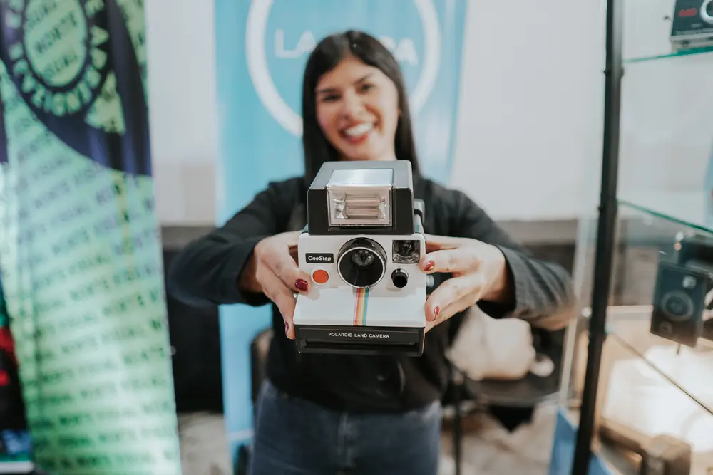 Una expositora sonríe y muestra una cámara instantánea en su stand de la ExpoFoto